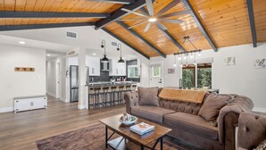 A spacious living area with a high ceiling, wooden beams, a large window, and a modern kitchen in the background.