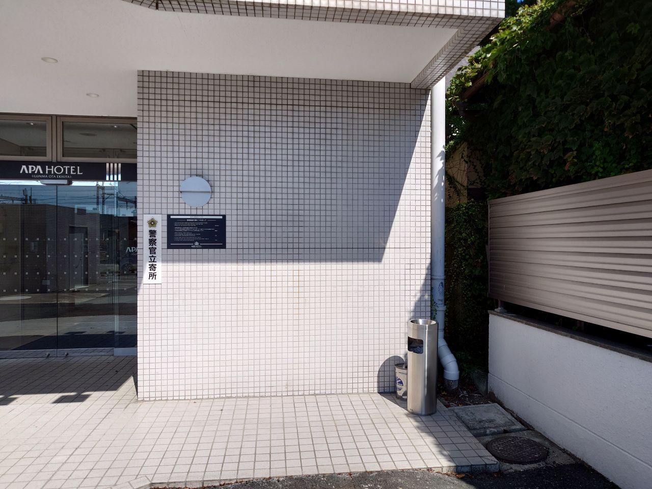 Un edificio con fachada de baldosas, una placa y un bote de basura.