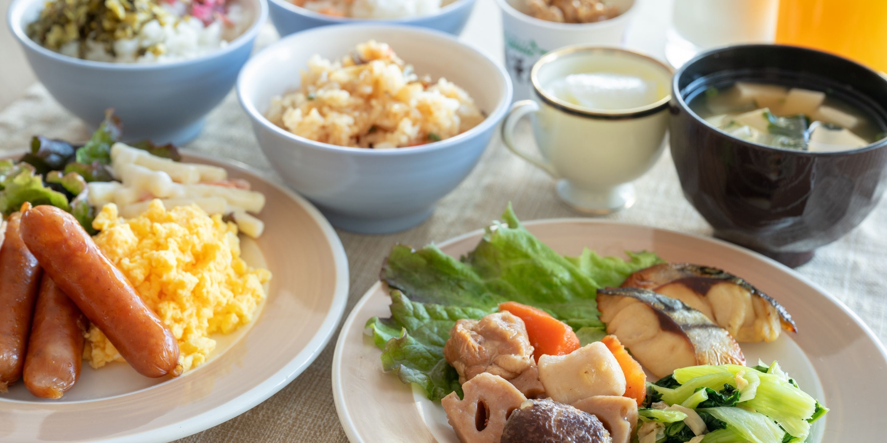 A table with various dishes including sausages, scrambled eggs, and vegetables.