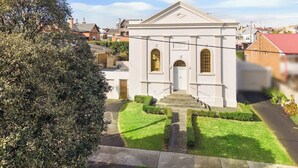 Un edificio bianco con una facciata simmetrica, un ingresso centrale e un piccolo giardino con un vialetto che conduce all'ingresso.