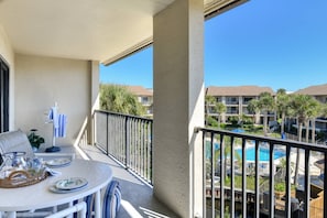 Un balcon avec une table dressée pour le dîner, une vue sur une piscine et un immeuble doté de nombreux balcons et de palmiers.