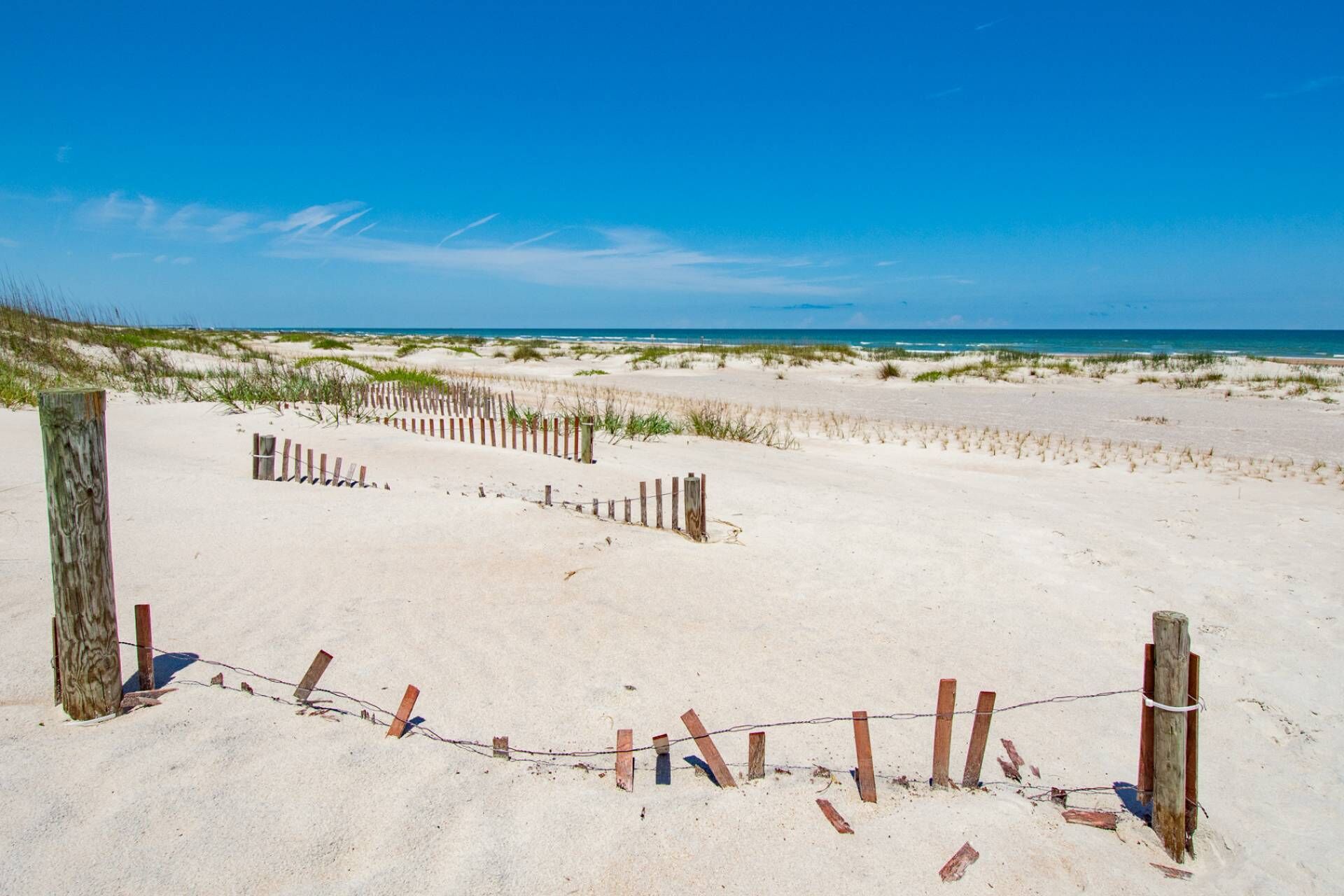 A sandy beach with a wooden fence and a clear blue sky.