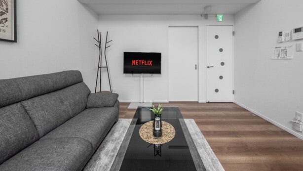 A modern living room with a grey sofa, a coffee table with a plant, a flat-screen TV, and a door with a green exit sign. - FURANO RESORT WAKABA D (Furano)