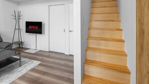 A modern living room with a wooden staircase, a flat-screen TV, and a coat rack. - FURANO RESORT WAKABA D (Furano)