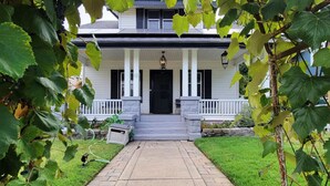A two-story house with a front porch, a stone bench, and a pathway leading to the entrance. - Rosewood Landing- Hot tub & Sauna- Sleeps 10 (Medford)