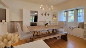 A dining area with a wooden table, cushioned chairs, a chandelier, and a view of the outdoors through large windows. - Rosewood Landing- Hot tub & Sauna- Sleeps 10 (Medford)