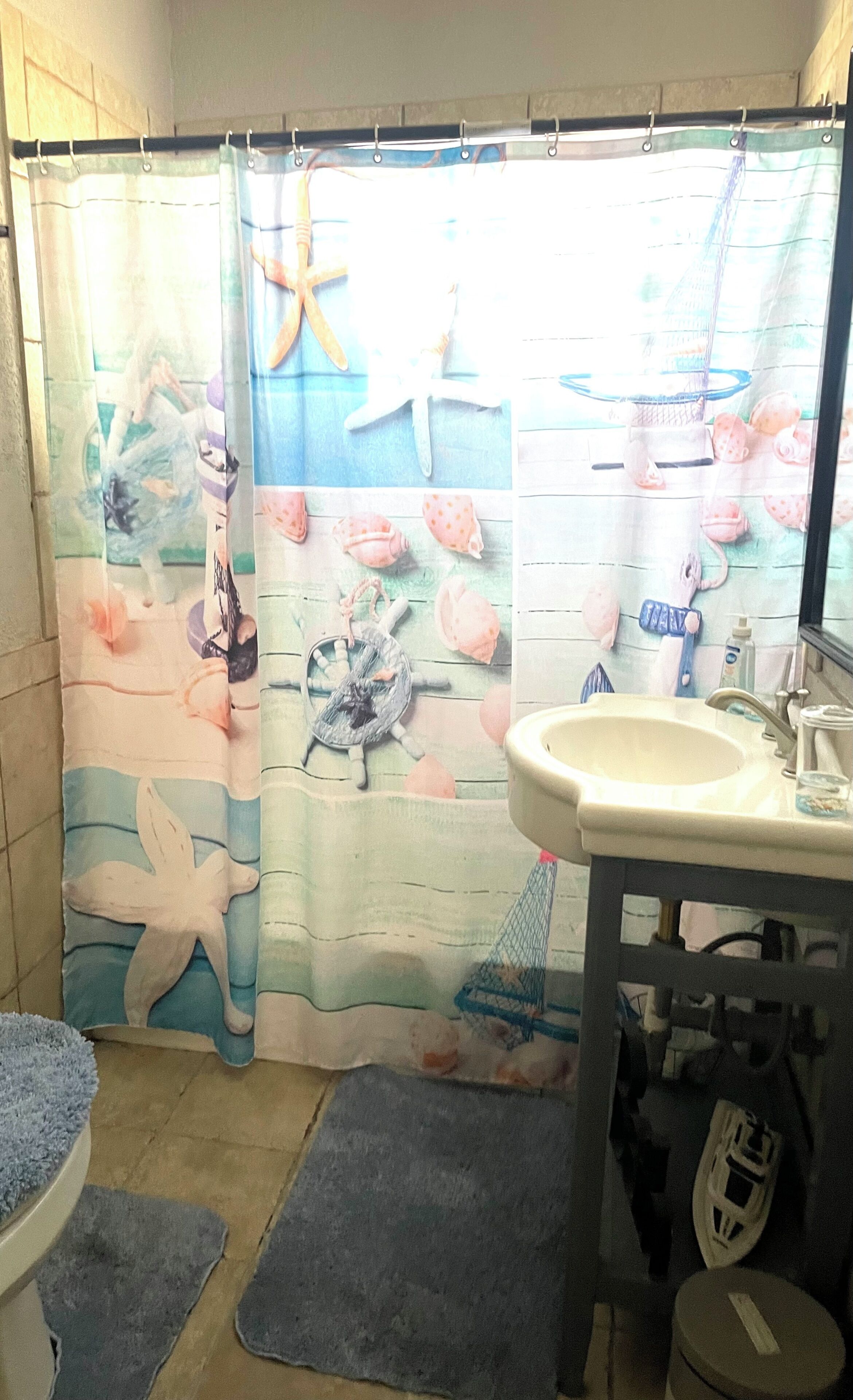 Un baño con cortina de ducha decorada con criaturas marinas, un lavamanos y un inodoro.