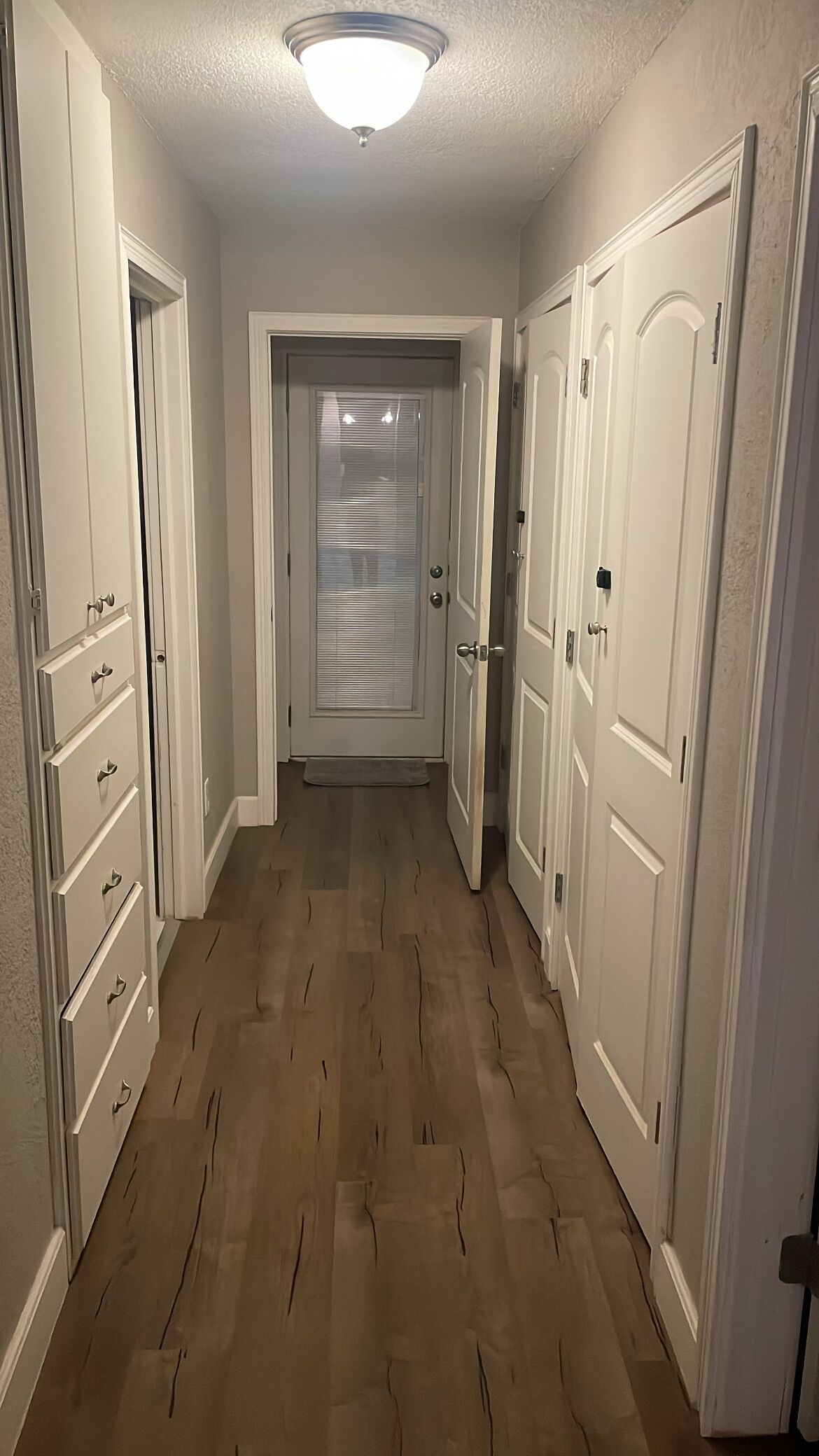 A hallway with wooden flooring, white doors, and a ceiling light fixture.