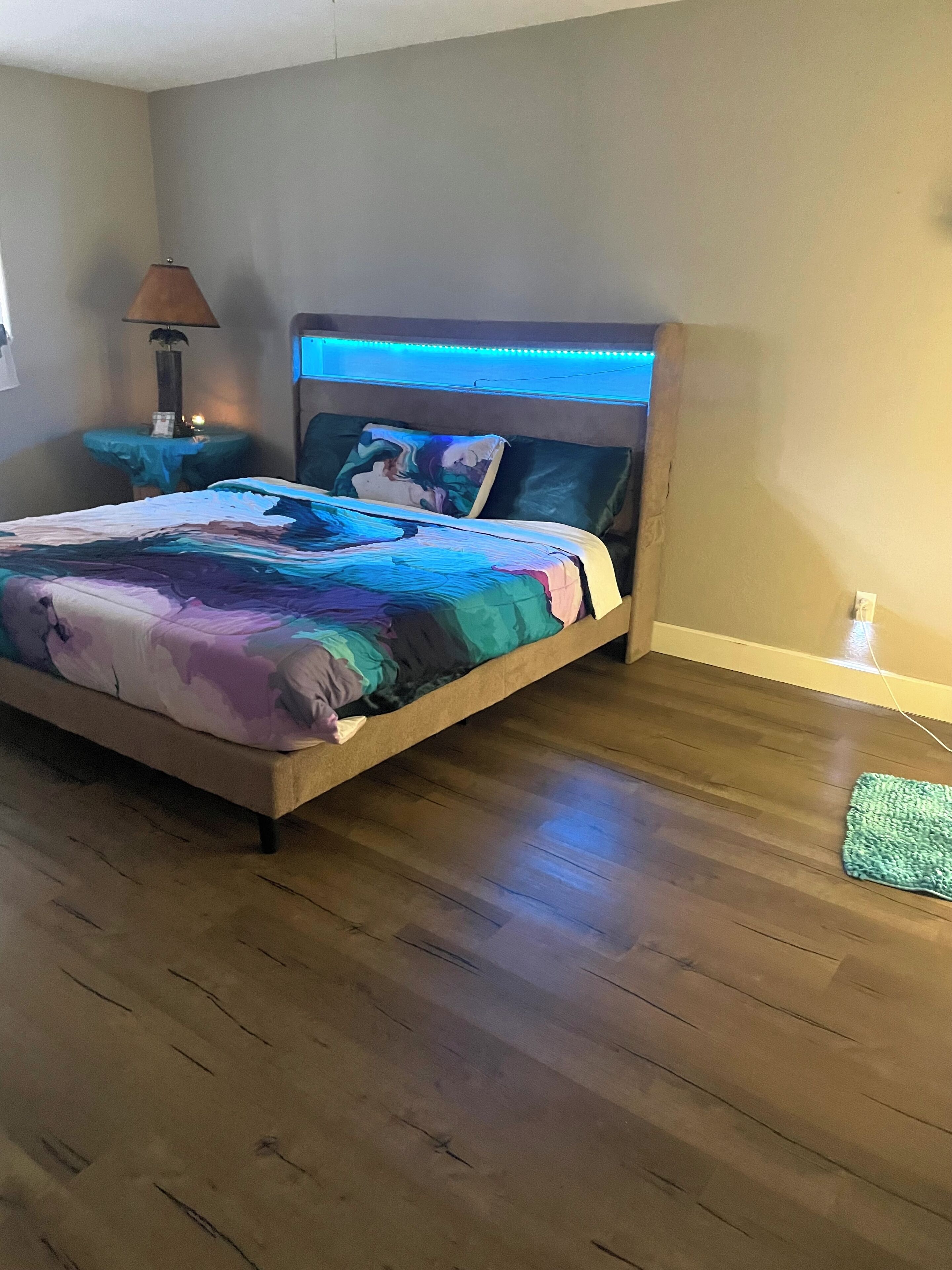 Un dormitorio con cama, mesita de noche, lámpara y alfombra verde.
