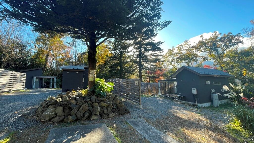 A gravel driveway leading to a building with a wooden fence and a tree in the foreground.