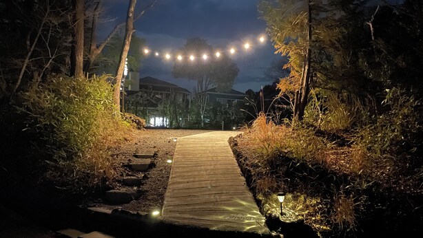 A wooden pathway leading to a building, surrounded by trees and illuminated by string lights. - Izu-Kogen Tent Resort (Ito)