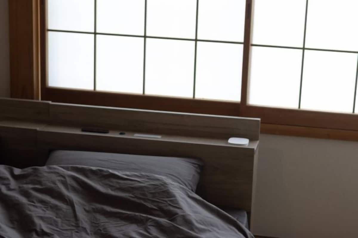 A bedroom with a wooden headboard, a bedside table, and a window with a grid pattern.