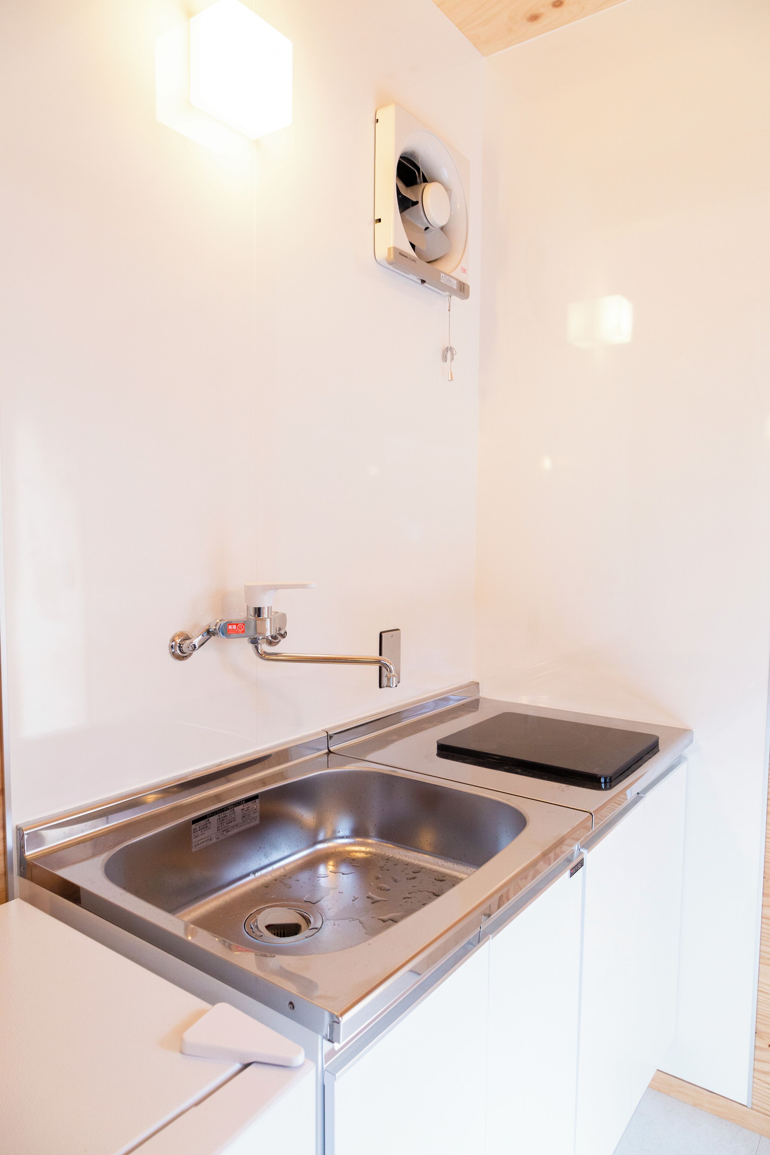 Una cocina moderna con un lavamanos de acero inoxidable, un horno empotrado y un ventilador de pared.