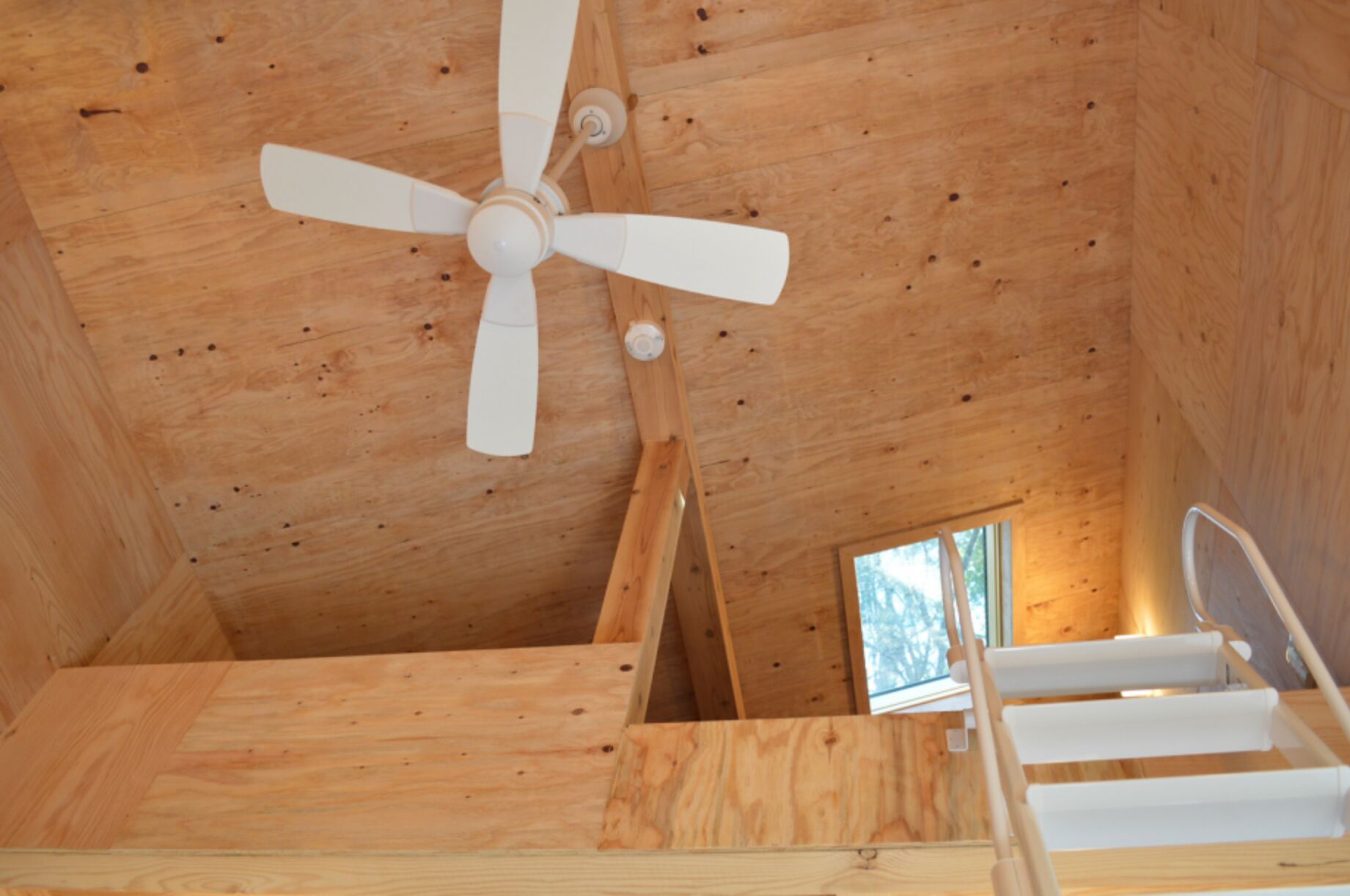 A wooden interior with a ceiling fan, a staircase, and a window.
