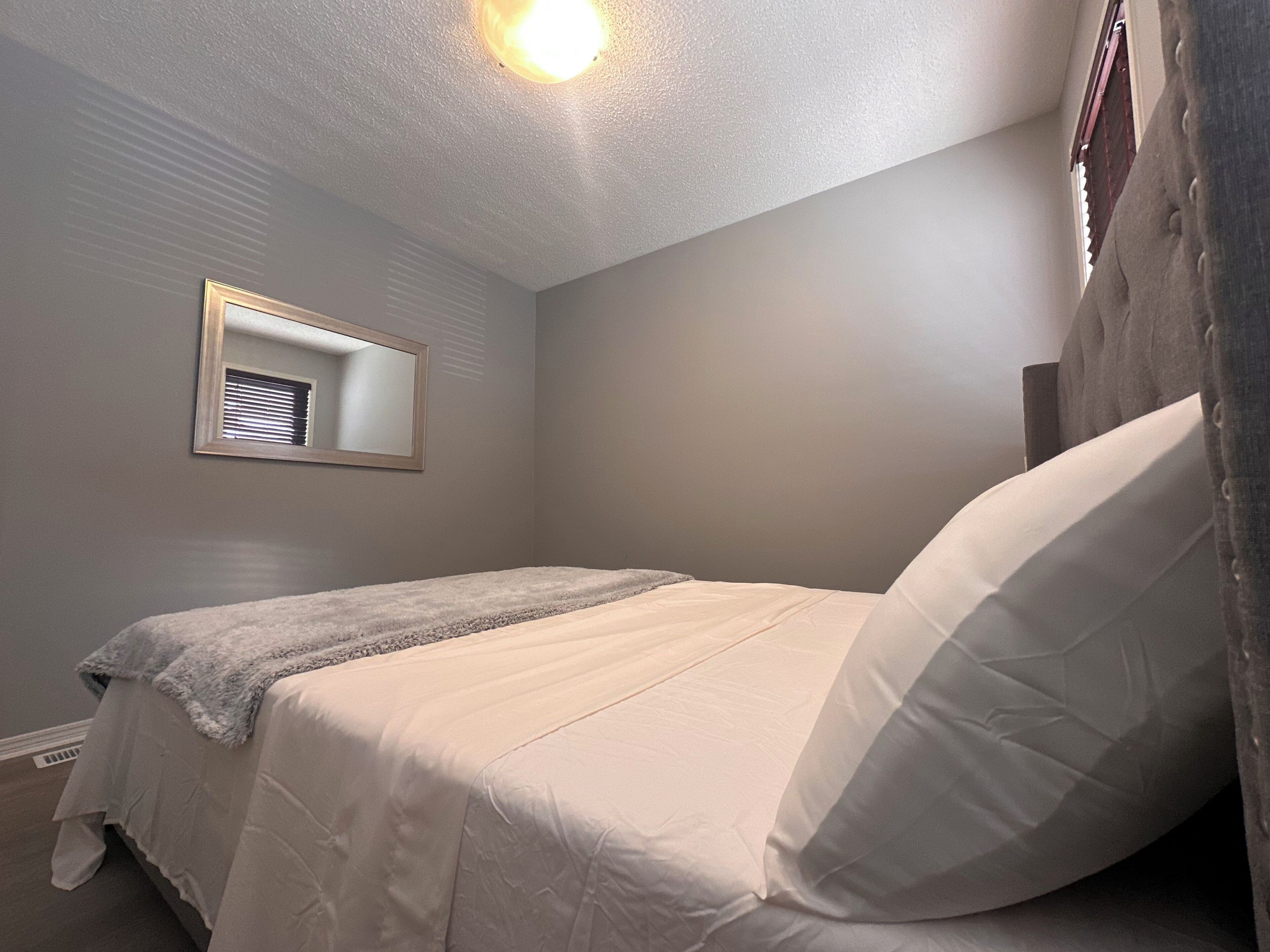 A bedroom with a bed, a window with blinds, and a ceiling light.