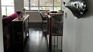 Ein modernes Wohnzimmer mit Holzboden, einem Essbereich mit Tisch und Stühlen sowie einem großen Fenster mit blauen Vorhängen.