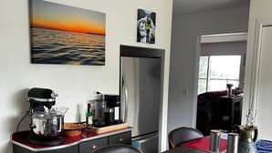 Eine kleine Küche mit Kühlschrank, Kaffeemaschine und einem Holztisch mit Unterlage.