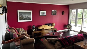 Ein Wohnzimmer mit roter Wand, einer Couch, einem Holztisch und einem Fenster mit Blick auf Bäume.