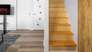 Un interior moderno con una escalera de madera, una puerta blanca y un televisor de pantalla plana mostrando 'NETFLIX'.