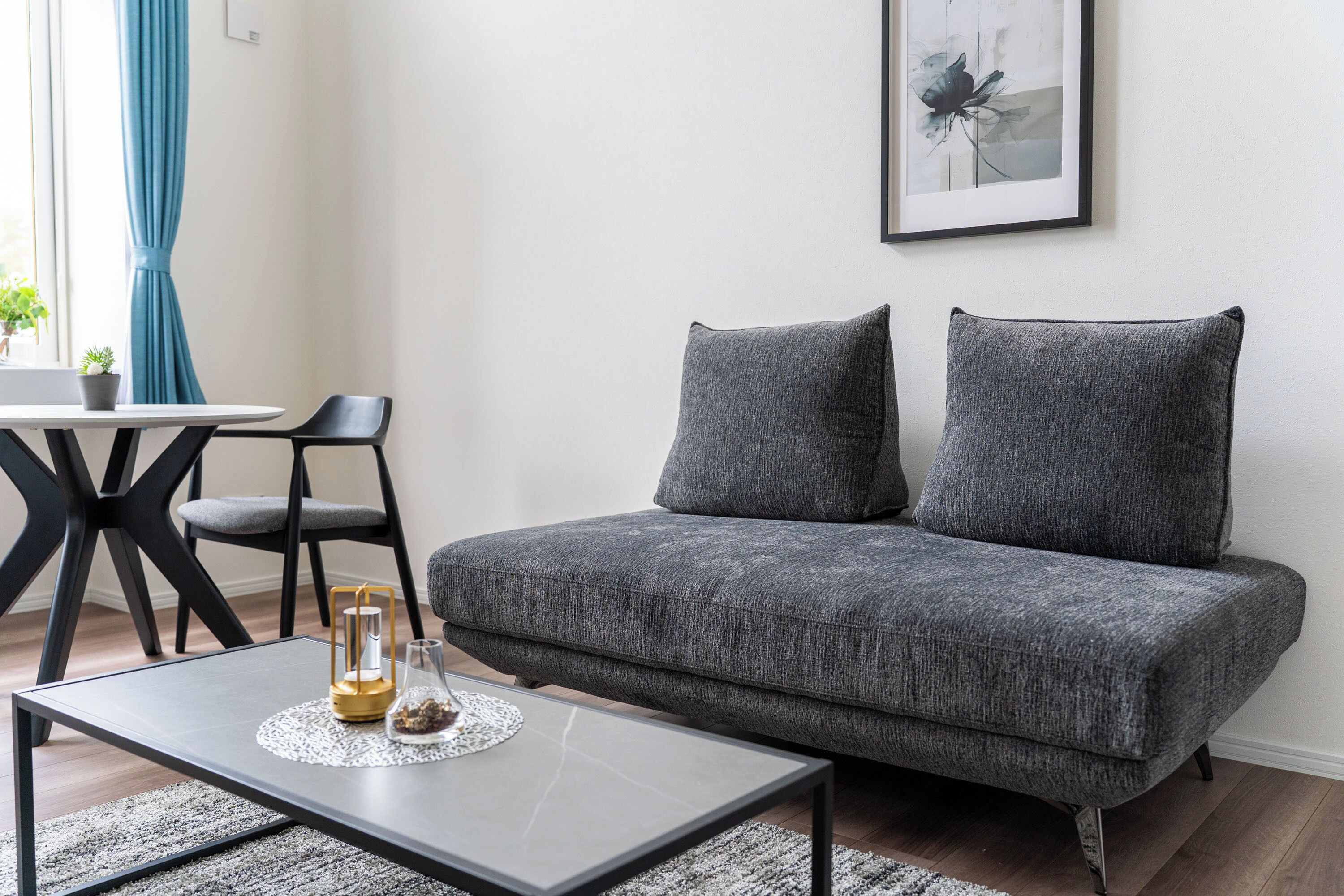 A modern living room with a grey sofa, a small table with a candle, and a chair.