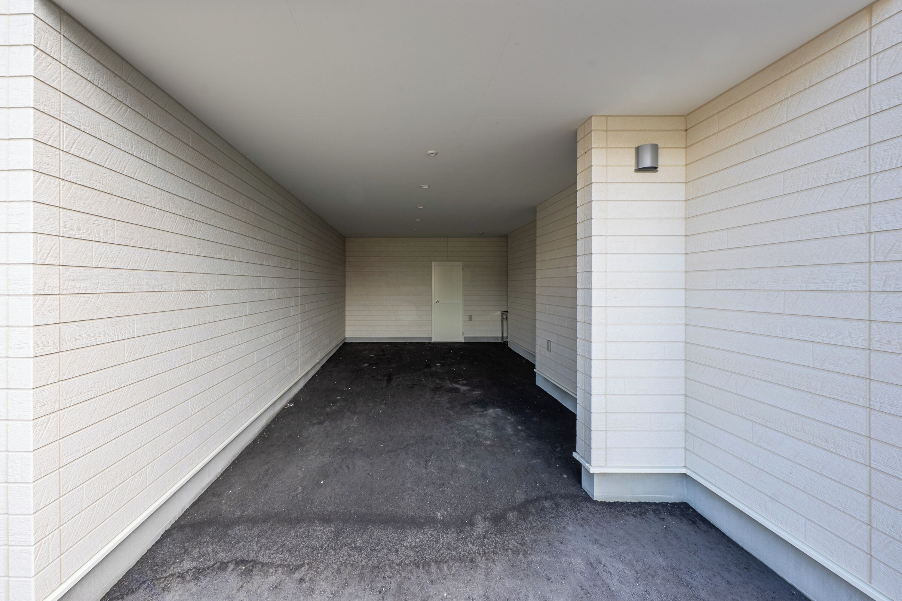 A narrow, enclosed hallway with white panel walls and a dark floor.