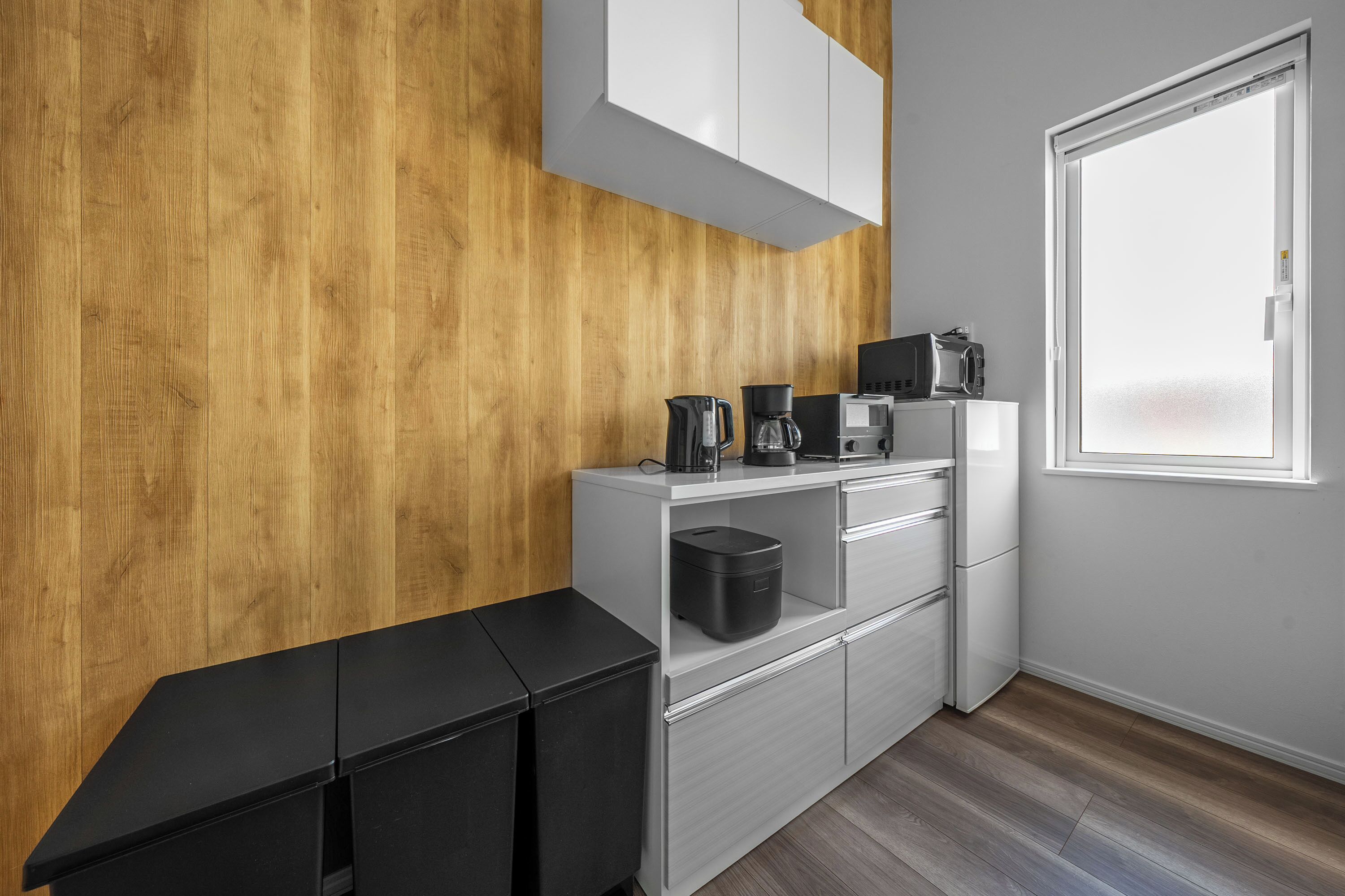 A modern kitchen with wooden paneling, a white countertop, and a window.
