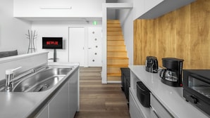 Cocina moderna con un lavamanos de acero inoxidable, cafetera y microondas. Una escalera de madera conduce a otro nivel.