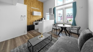 Un apartamento moderno con cocina, comedor y sala de estar. Cuenta con una pared de acento de madera, una mesa de comedor con sillas, un sofá y una mesa de centro.