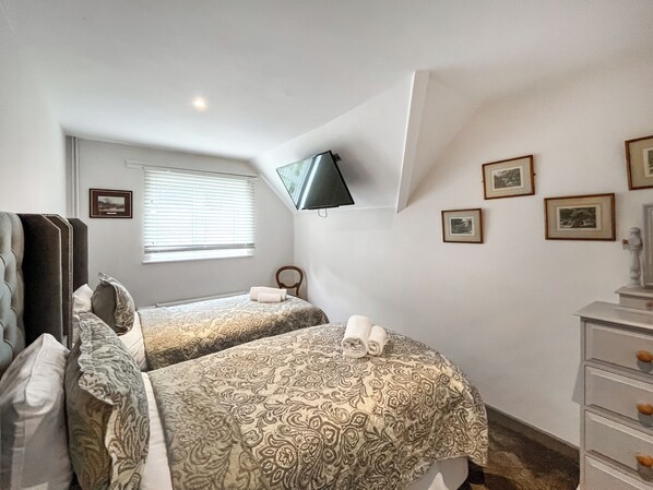 A bedroom with two beds, a dresser, a TV mounted on the wall, and several framed pictures.