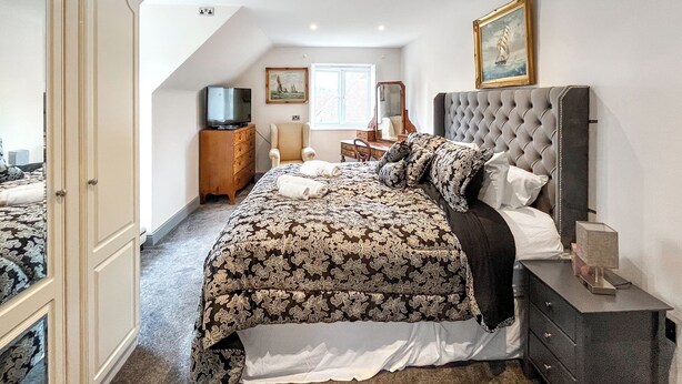 Une chambre à coucher avec un grand lit, une commode, une coiffeuse, un téléviseur et un tableau accroché au mur.