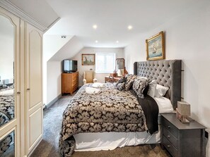 A bedroom with a large bed, a dresser, a vanity, a television, and a painting on the wall.