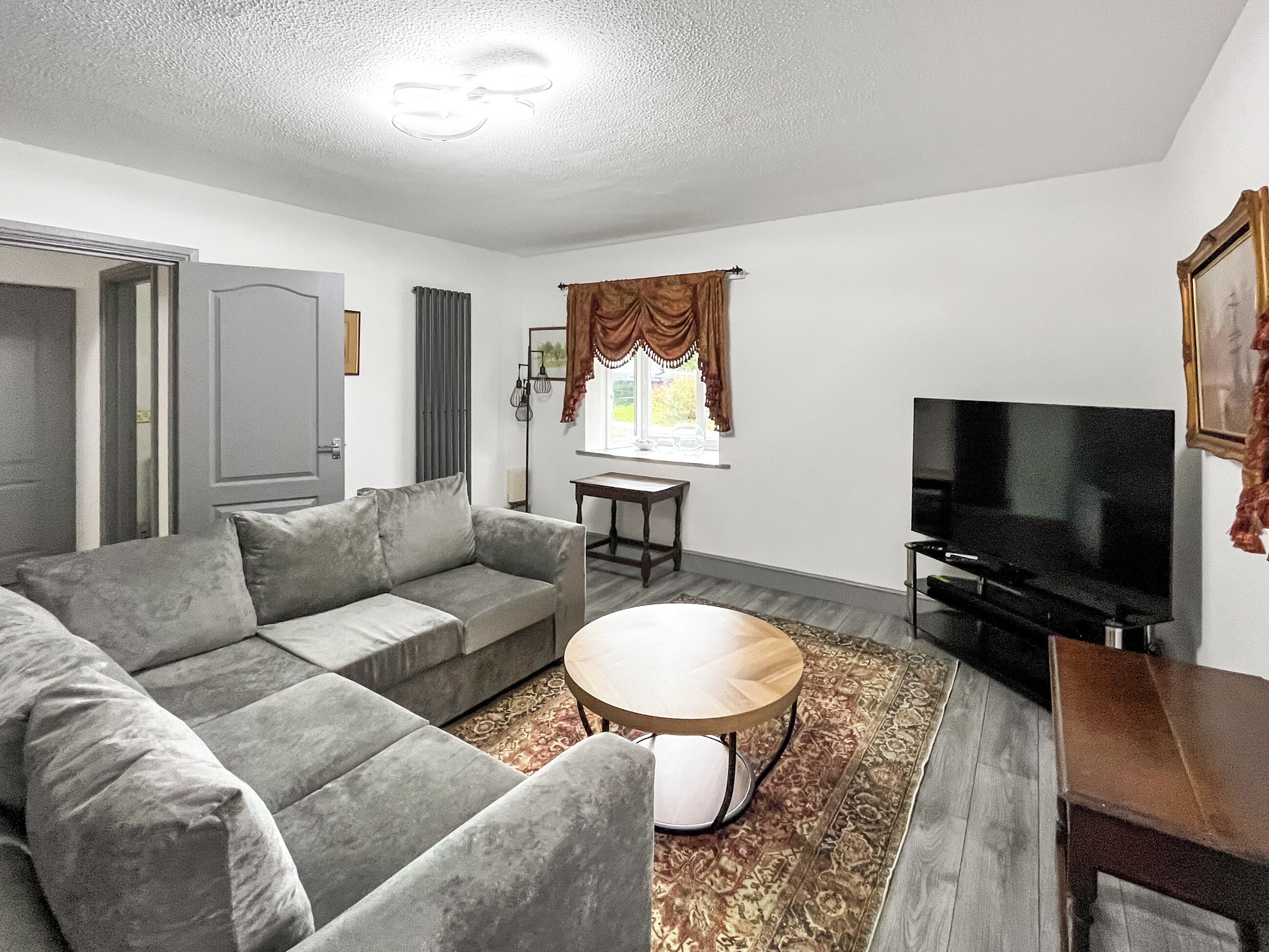 A living room with a sofa, a coffee table, a television, and a window with curtains.