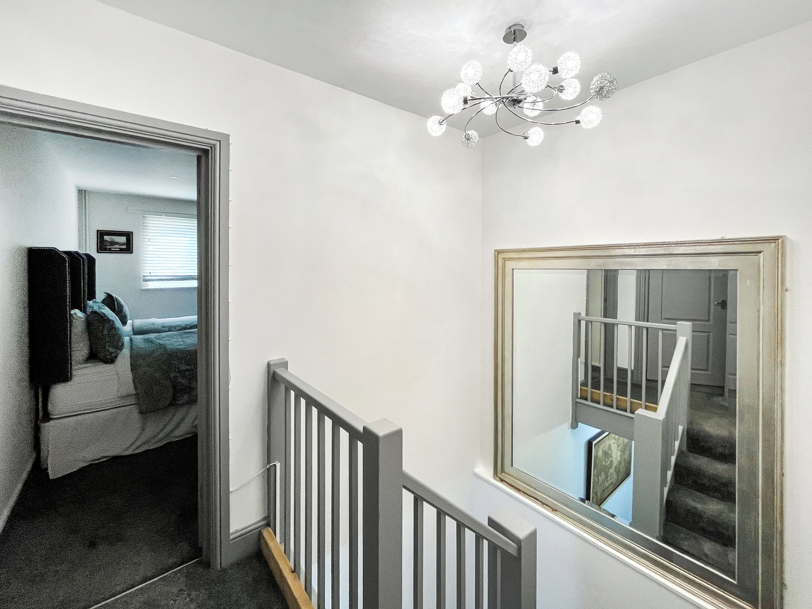 A staircase with a white railing, a chandelier, and a large mirror on the wall.