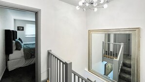 Un escalier avec une rampe blanche, un lustre et un grand miroir au mur.