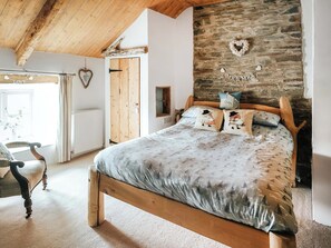 Une chambre avec un mur en pierre, un lit avec une literie à motifs, une tête de lit en bois et une chaise en bois.