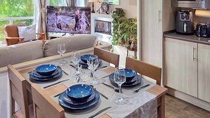 A dining area with a table set for four, a television in the background, and a kitchen area with appliances.
