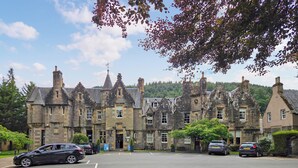 A historic stone building with multiple chimneys and a clock tower. - 2 bedroom accommodation in Birnam (Birnam)