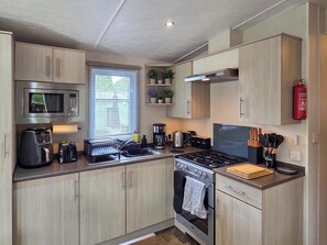 A modern kitchen with stainless steel appliances, wooden cabinets, a window with blinds, and a fire extinguisher on the wall. - 2 bedroom accommodation in Birnam (Birnam)