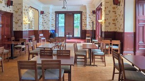 A dining area with wooden tables and chairs, patterned wallpaper, and a large window with blinds. - 2 bedroom accommodation in Birnam (Birnam)