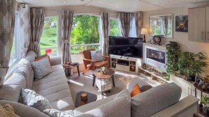 A modern living room with a large sofa, a flat-screen TV, and a fireplace. - 2 bedroom accommodation in Birnam (Birnam)