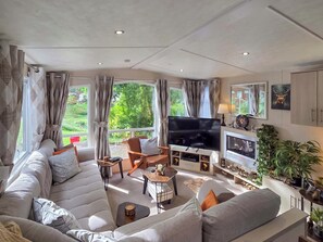 A modern living room with a large sofa, a flat-screen TV, and a fireplace. - 2 bedroom accommodation in Birnam (Birnam)