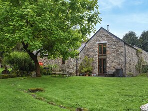 A stone building with a large door, a grassy yard, and a tree.