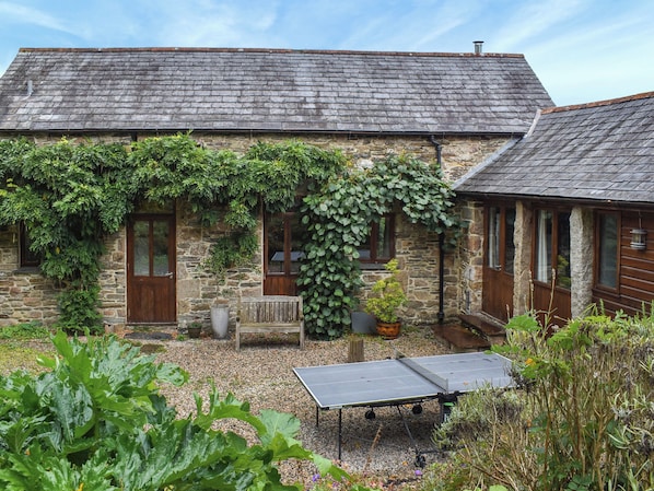 A stone building with a sloped roof, a wooden door, and a small garden area with a ping pong table.