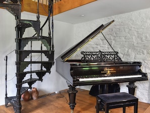 A grand piano with a black finish and gold accents, positioned in a room with a white brick wall and wooden flooring. - 3 bedroom accommodation in Liskeard (Liskeard)