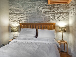 Ein Bett mit Holz Kopfteil, zwei Nachttischlampen und einer Wand mit strukturierter Steinoptik.