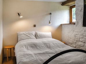 A bedroom with a bed, two wall-mounted lights, a small stool, and a window with a view of trees. - 3 bedroom accommodation in Liskeard (Liskeard)