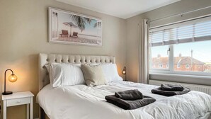 A neatly made bed with white linens, a headboard, and two bedside lamps. - Spacious family home with games, a private hot tub and coastal adventures. (Whitby)