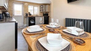 A dining area with a table set for four, a washing machine, a microwave, and a television in the background. - Spacious family home with games, a private hot tub and coastal adventures. (Whitby)