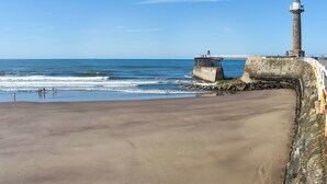 A sandy beach with a stone wall and a lighthouse in the background. - Spacious family home with games, a private hot tub and coastal adventures. (Whitby)