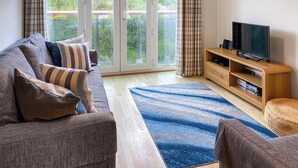 A living room with a sofa, TV, wooden entertainment unit, and a view through a glass door. - 1 bedroom accommodation in Newquay (Newquay)